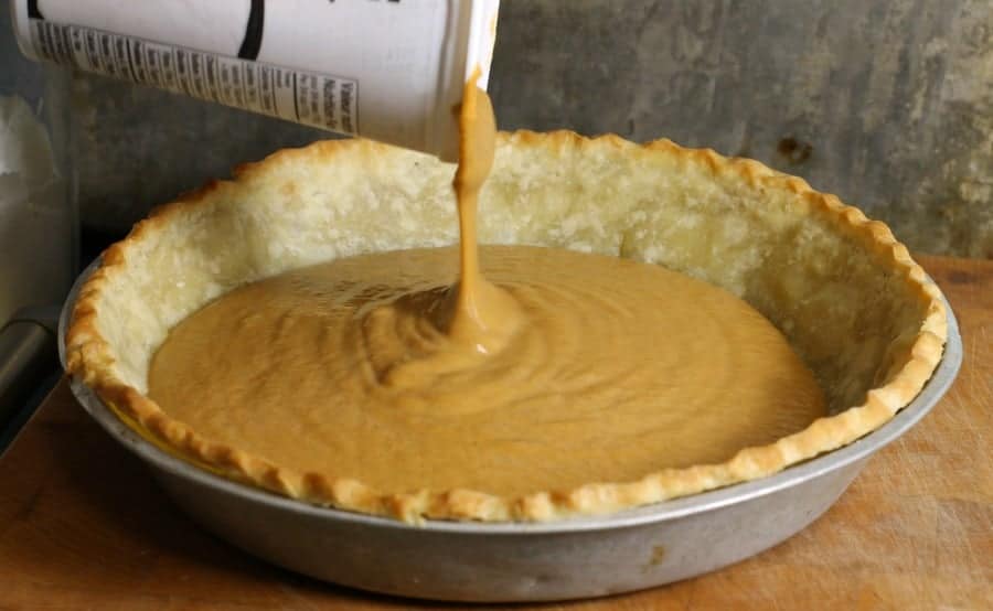 Pumpkin pie filling being poured into a blind baked pie crust