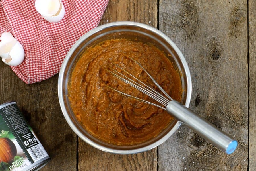 an overhead shot of a mixing bowl on a wooden table, filled with pumpkin puree