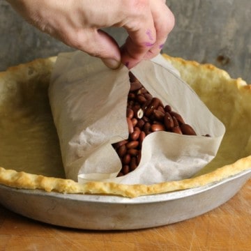 beans used as pie weights being removed from a pie crust