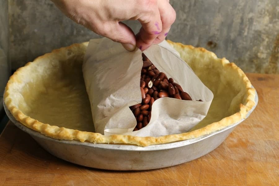 beans used as pie weights being removed from a pie crust