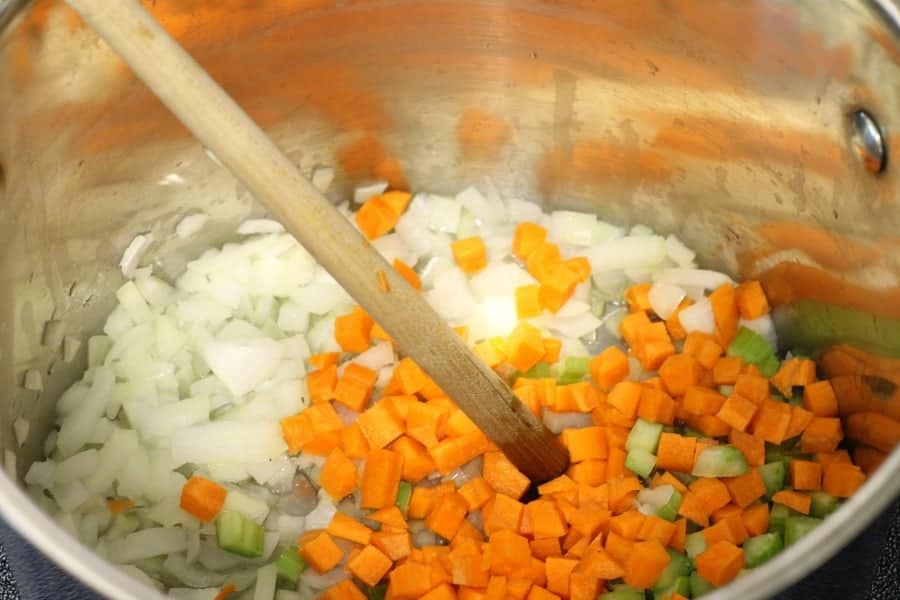 onions, carrot, and celery being sauteed in a pot with oil.