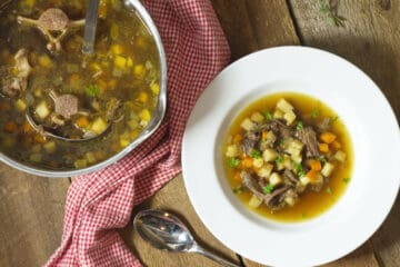 a top down shot of a pot of broth based oxtail soup beside a white rimmed bowl of oxtail soup