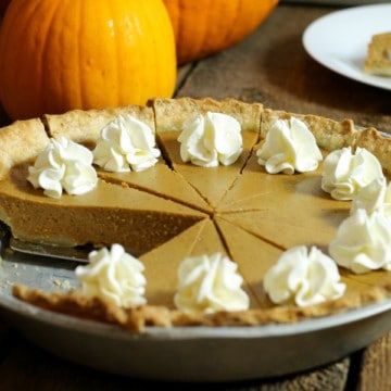 A sliced and garnished homemade pumpkin pie made from scratch, sitting on a wodden table . one pice of pie has been removed.