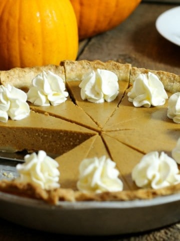 A sliced and garnished homemade pumpkin pie made from scratch, sitting on a wodden table . one pice of pie has been removed.
