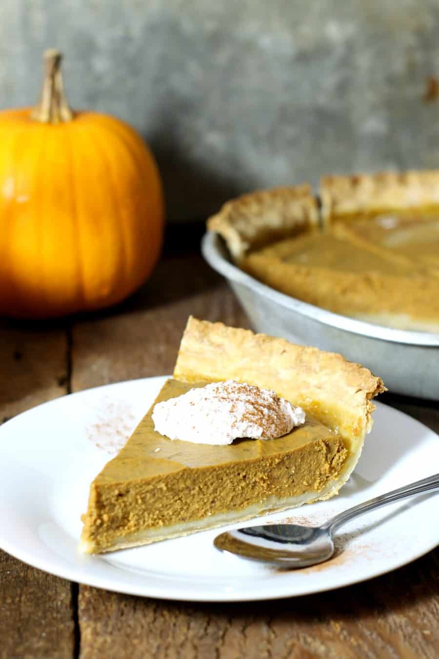 a vertical image of a dairy free slice of pumpkin pie on a white plate garnished with cinnamon