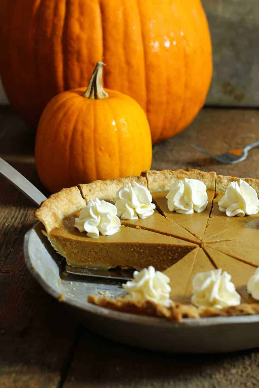 a vertical image of a cut and garnished punpkin pie in a pie pan with one piece removed
