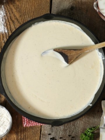 overhead shot of bechamel sauce in a cast iron pan, surrounded by various ingredients.