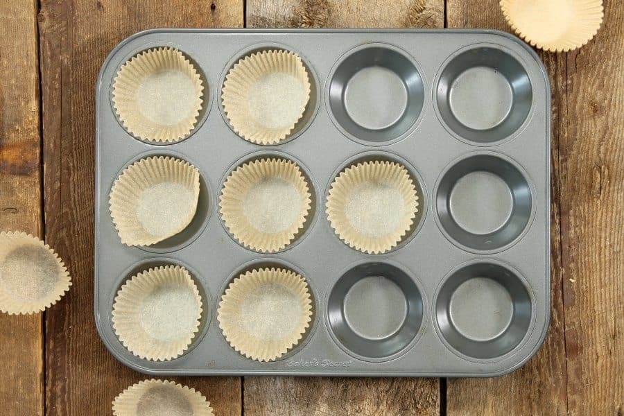 a grey muffin tin being lined with parchment paper muffin liners