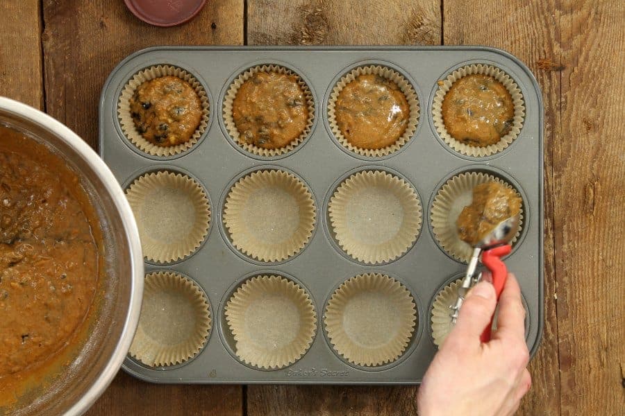 blueberry bran muffin batter being portioned into a lined muffin tin with a red handled ice cream scoop