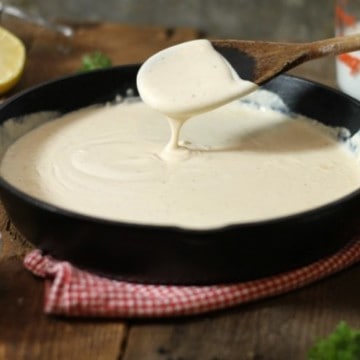 thickened bechamel sauce dripping of a wooden spoon into a cast iron pan