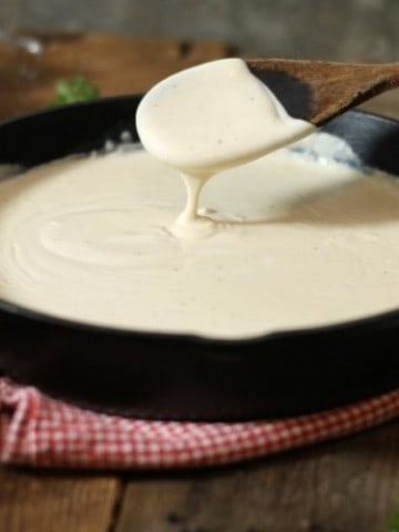 thickened bechamel sauce dripping of a wooden spoon into a cast iron pan