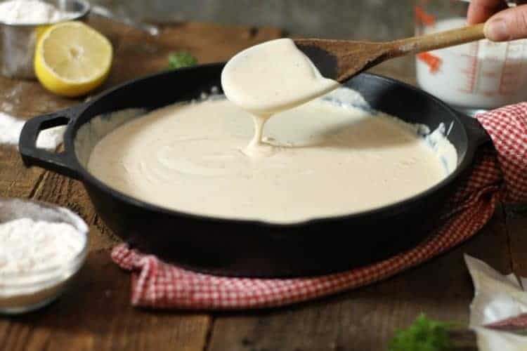 thickened bechamel sauce dripping of a wooden spoon into a cast iron pan