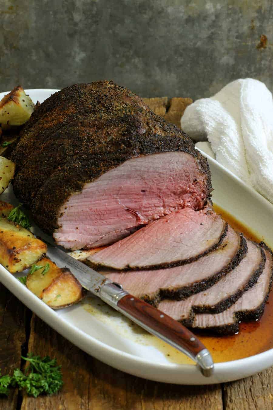 vertical image of a sliced sirloin tip roast crusted with coffee on a white serving platter