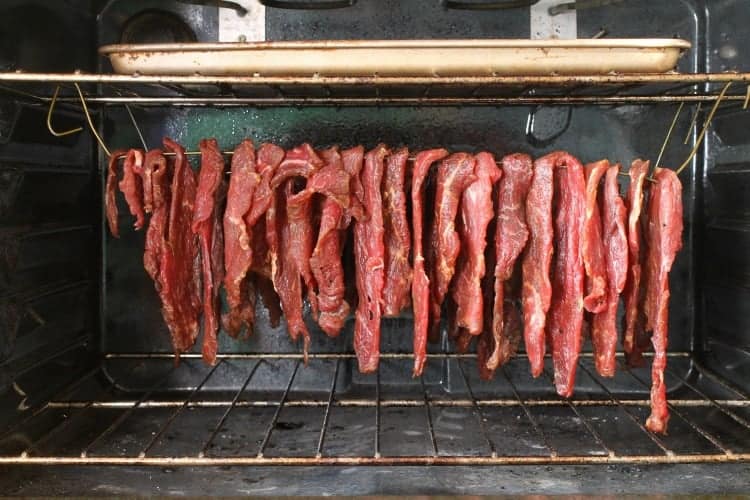 raw beef jerky strips hanging in an oven to dry