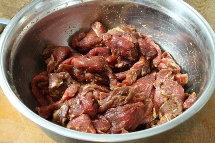 sliced raw beef strips marinading in a steel bowl