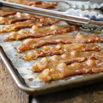 close up of perfectly cooked oven baked bacon strips on a parchment lined sheet pan