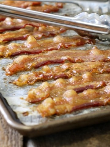 close up of perfectly cooked oven baked bacon strips on a parchment lined sheet pan