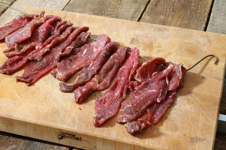 raw beef jeerky strips being threaded onto a wire for drying