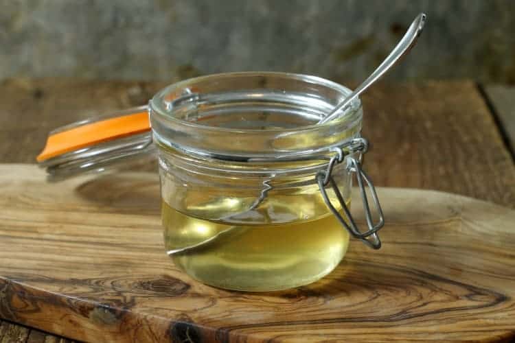 a glass jar of rendered bacon fat on an olive wood board