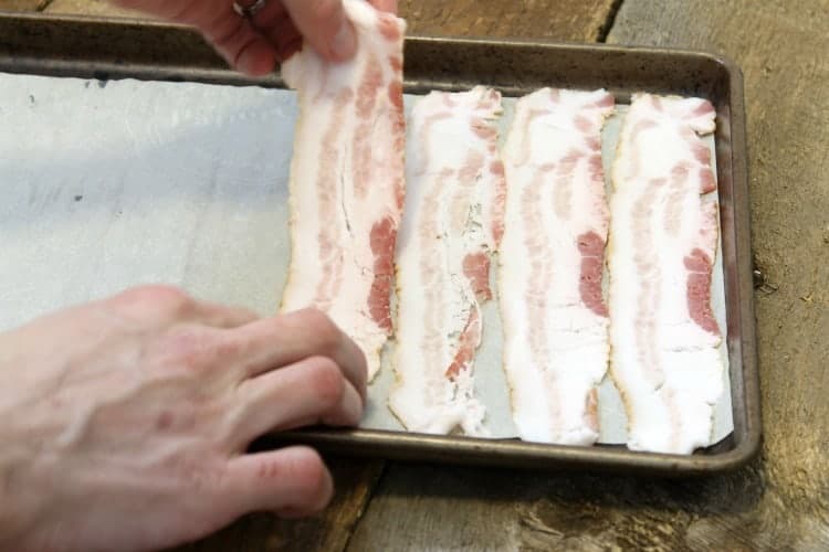 traying up raw bacon slices on a parchment lined sheet pan