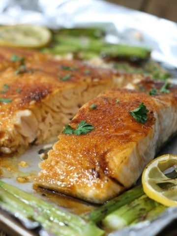 Brown sugar glazed salmon on a tinfoil lined pan surrounded by asparagus