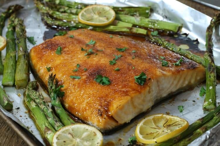 brown sugar glazed baked salmon on a sheetpan after cooking surrounded by asparagus and lemon slices