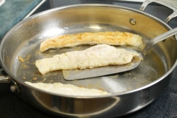 flipping pan fried haddock with a metal spatula