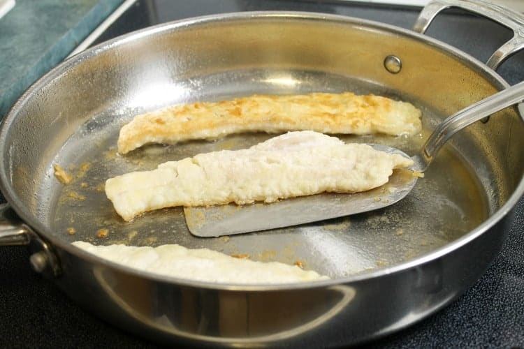 flipping pan fried haddock with a metal spatula