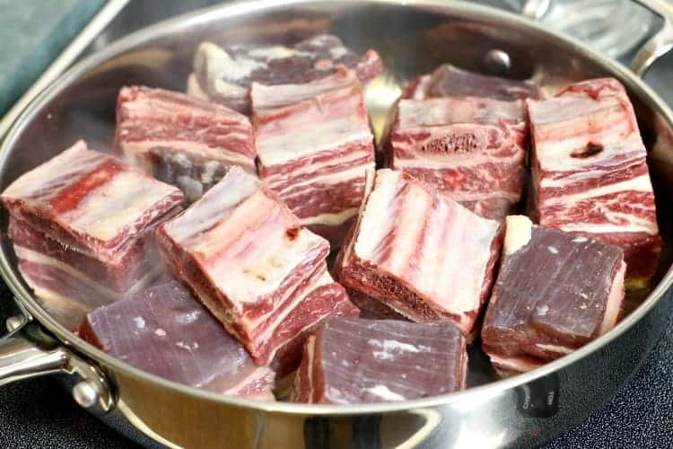 raw beef short ribs being pan seared in a metal pan