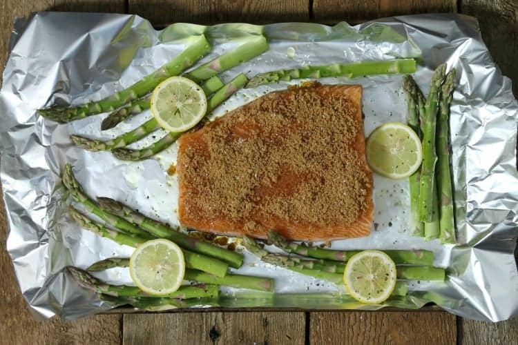 lemon slices and asparagus surrounding a raw pice of salmon on a sheet pan