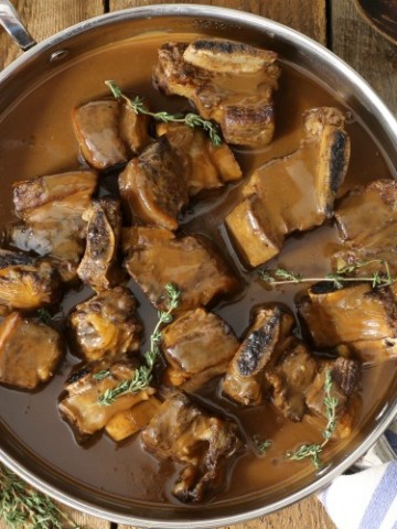 Top down view of red wine braised short ribs in a large pan on a wooden table top