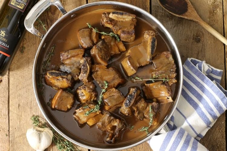 Top down view of red wine braised short ribs in a large pan on a wooden table top