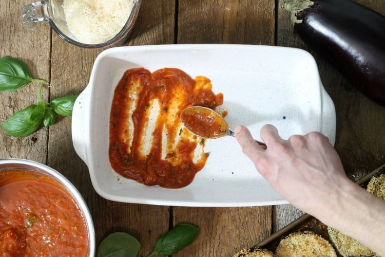 spreading tomato sauce in the bottom of the casserole dish