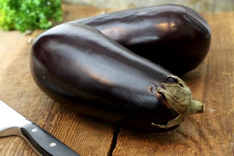 Two deep purple eggplants on a barn board table