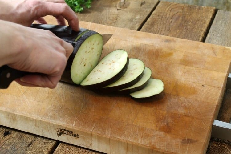 eggplant being cut into slices on a wooden cutting board