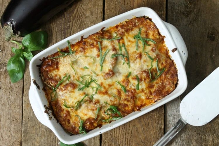 overhead view of a baked eggplanyt parmesan on a barn board table, surrounded by various ingredients