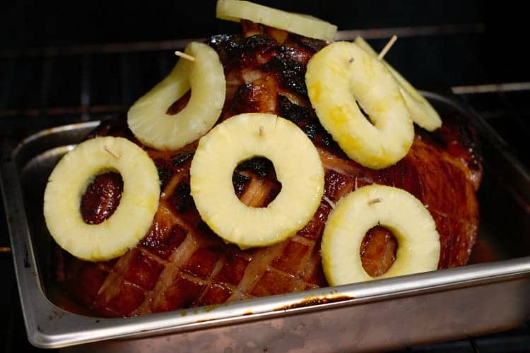 fresh pineapple slices pinned onto a glazed ham butt