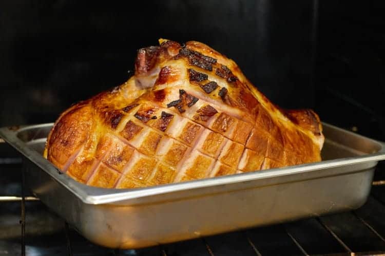 partially baked ham butt in a roasting pan with diagonally scored fat