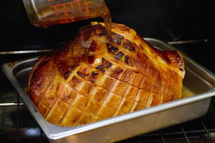 honey and pineapple glaze being poured over a partially baked ham butt