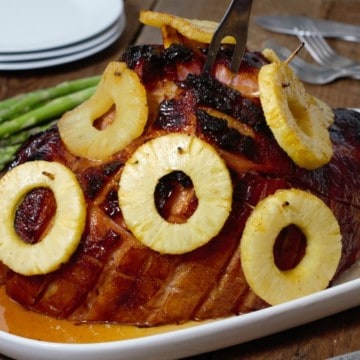 a honey a pineapple glazed ham on a serving platter with a carving fork stuck in the top