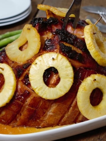 a honey a pineapple glazed ham on a serving platter with a carving fork stuck in the top