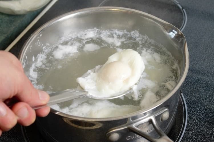 removing poached eggs with a slotted spoon from a pot of water
