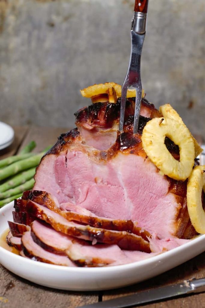 a sliced pineapple and homney glazed ham on a white platter