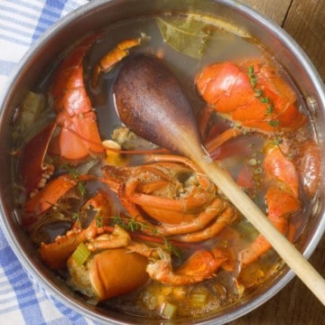 Lobster stock in a large pot with lobster shells, veg and a wooden spoon