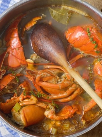 Lobster stock in a large pot with lobster shells, veg and a wooden spoon