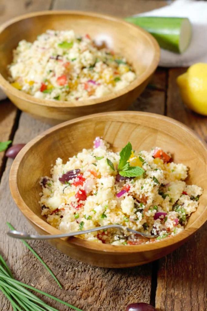 Mediterranean Couscous Salad being served in rustic olive wood bowls and garnished with fresh mint.