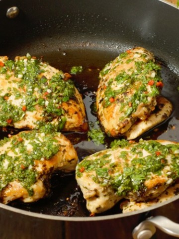 Pan seared chicken breasts topped with fresh chimichurri sauce in a pan