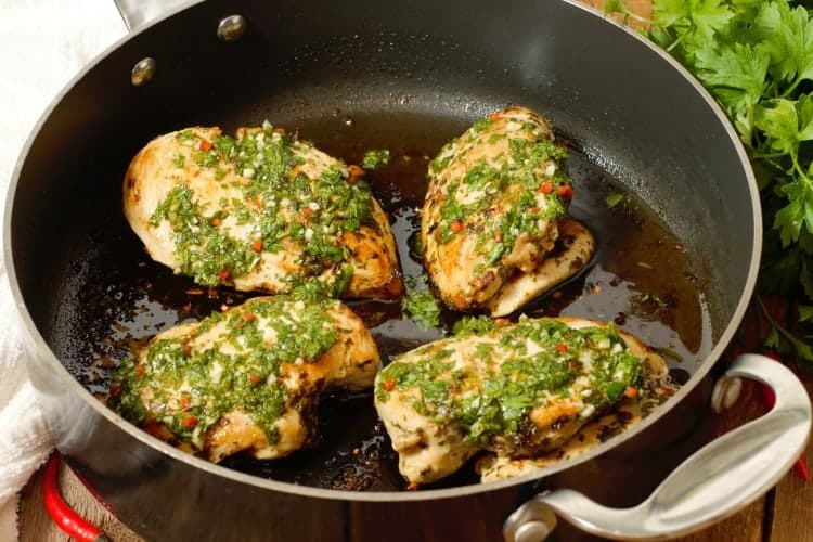 Pan seared chicken breasts topped with fresh chimichurri sauce in a pan
