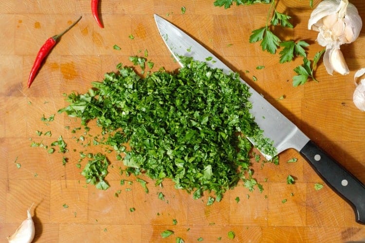 finely chopped parsley on a wooden cutting board with a chefs knife