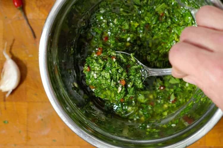 close up of chimichurri being spooned out of a steel bowl